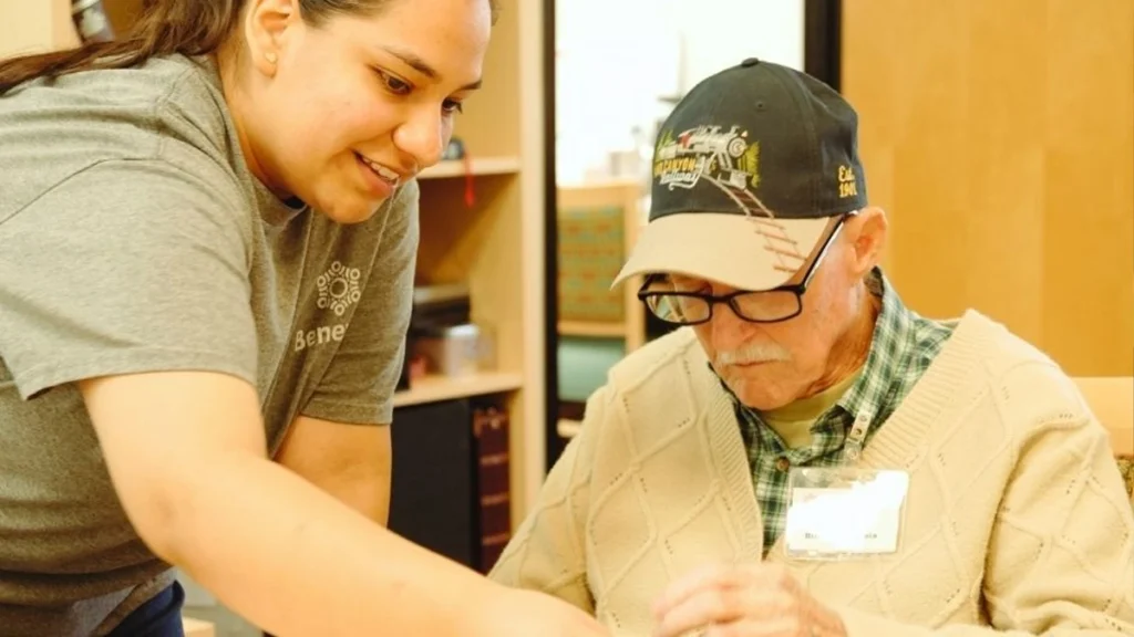 Benevilla staff member assisting a Life Enrichment Program participant during a hands-on activity, highlighting supportive engagement and meaningful connection.